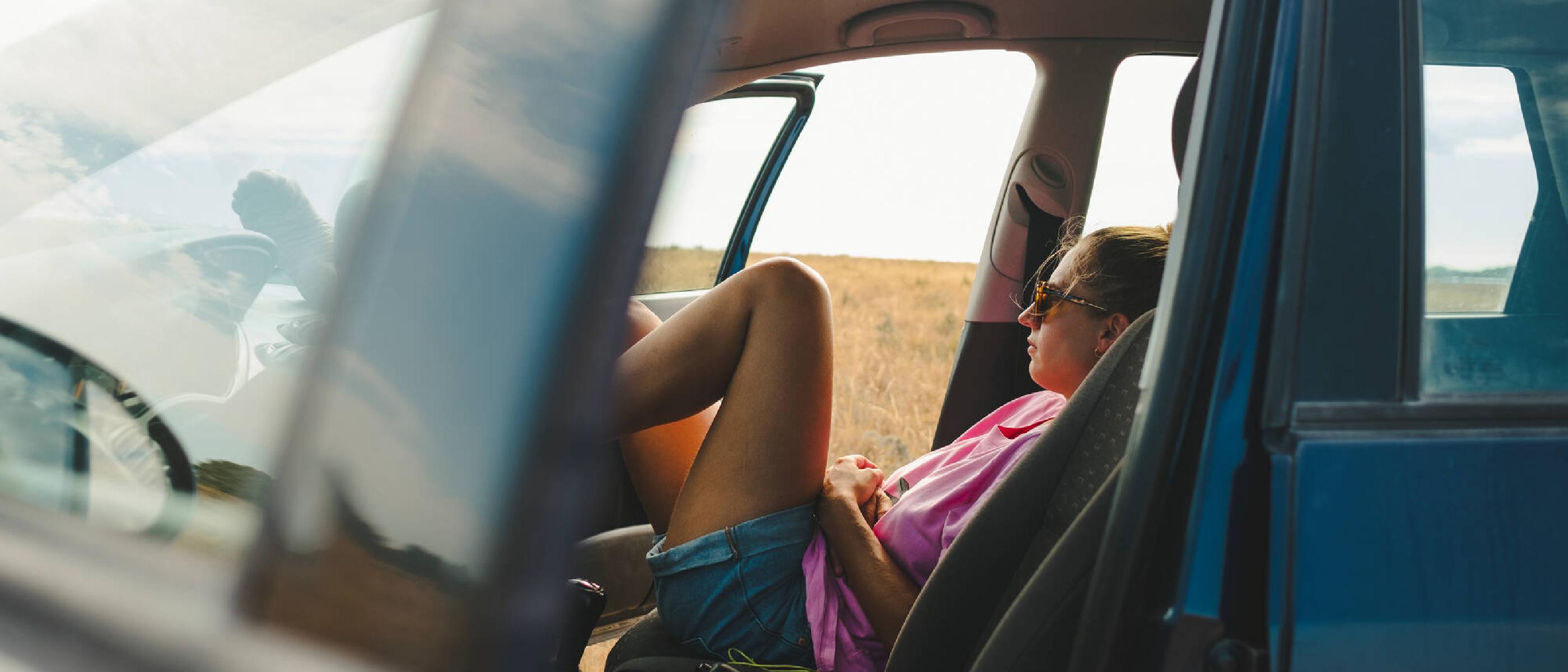 Ung kvinna sitter i bil med öppen  dörr