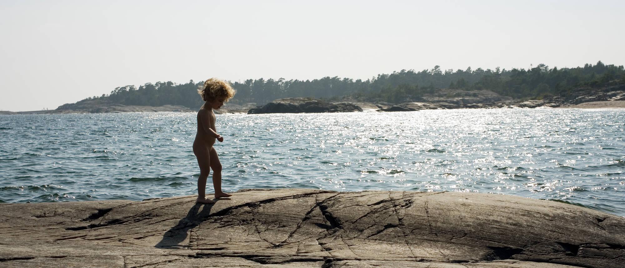 Litet barn går naken på klippor vid vatten