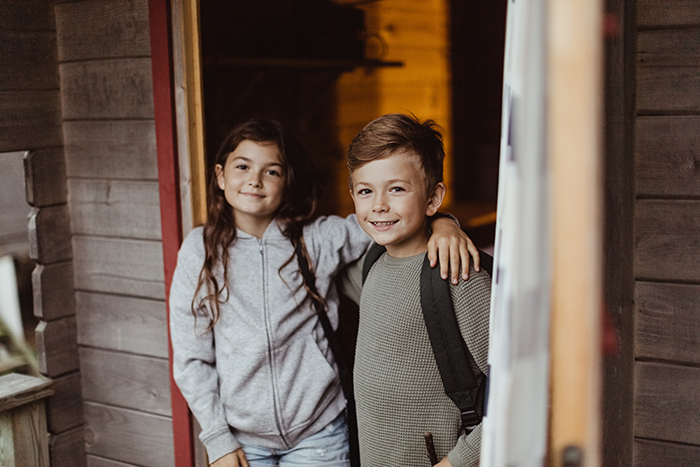 Flicka och pojke som står i dörren till en stuga