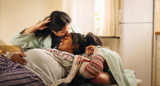 En gravid kvinna ligger ner och vilar och får en puss på hjässan av sin partner.