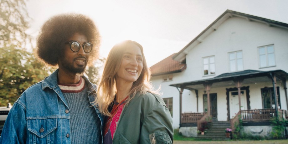 En man och en kvinna står utanför sitt nyinköpta hus och ler.