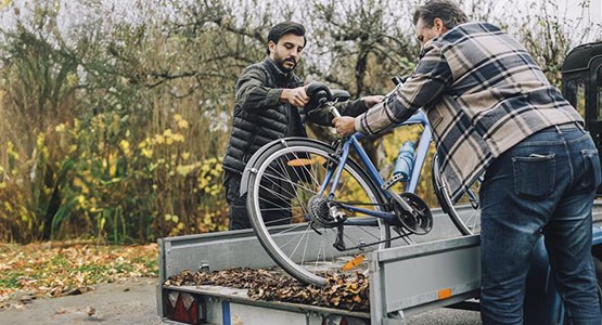 Två personer lastar cykel på släpvagn.