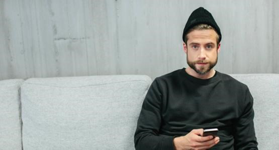 Man sitter i soffa med mobiltelefon i handen