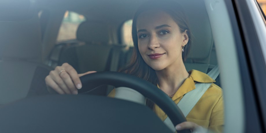 Kvinna som ler genom framrutan på sin bil.