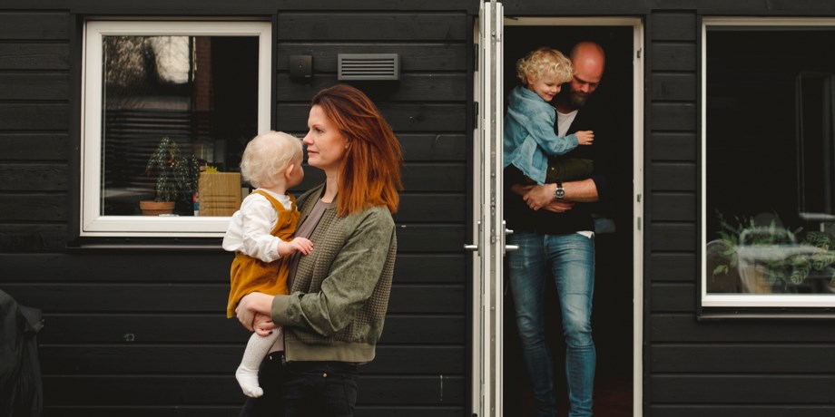 Mamma och pappa med var sitt barn i famnen går ut ur sitt hus.