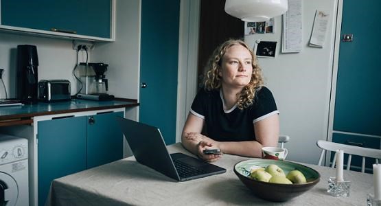 Ung kvinna sitter i köket och funderar.