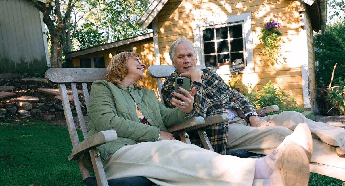 Par i medelåldern sitter i sin trädgård.