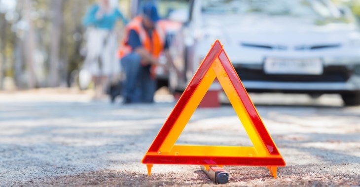 En varningstriangeln i förgrunden och i bakgrunden en person som byter däck på sin bil.