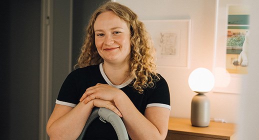 En ung kvinna står lutad mot en dammsugare och ler mot kameran.