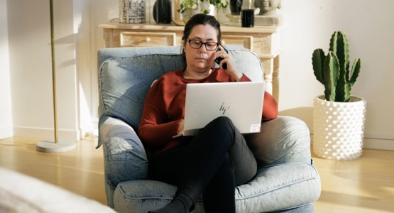 Medelålders kvinna sitter i fåtölj och arbetar på laptop.