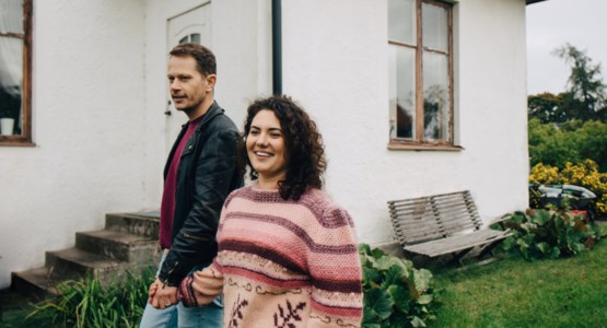 Par som håller hand framför ett hus