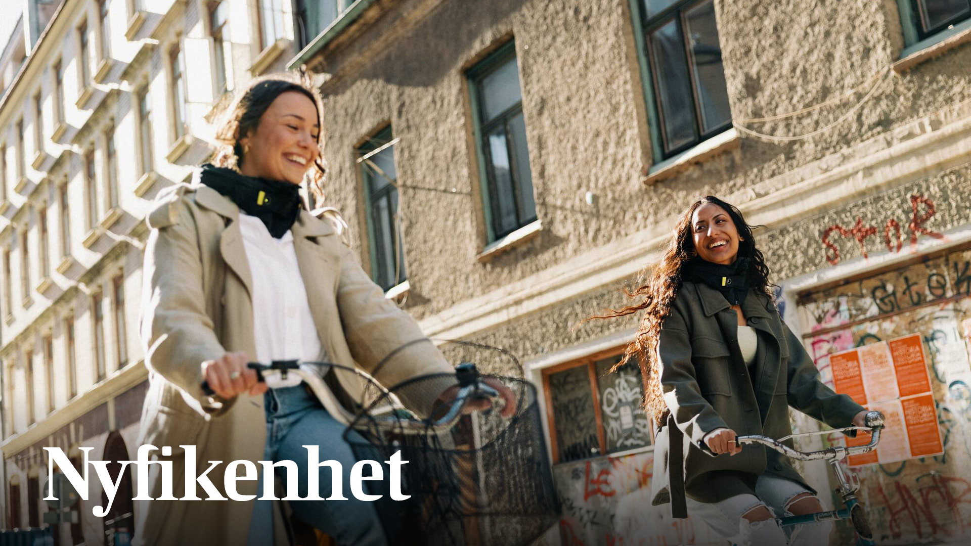 Två kvinnor cyklar i stadsmiljö och Nyfikenhet står skrivet intill kvinnorna.