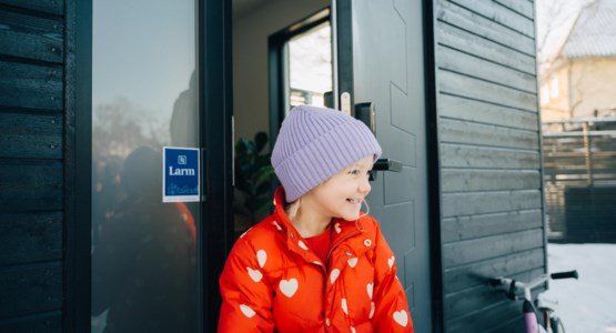 Flicka står vid ytterdörren med en larmskylt på fasaden.