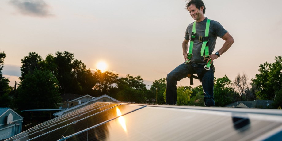 En man står på ett villatak och inspekterar solceller.