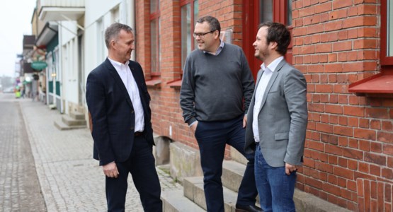 Tre män står och samtalar utanför byggnad i stadsmiljö.