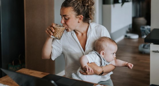 Kvinna arbetar vid laptop med bebis i knät.