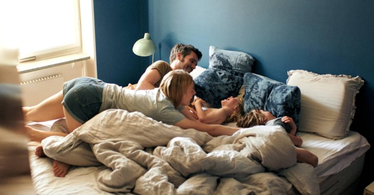 Familj leker och busar i sängen.