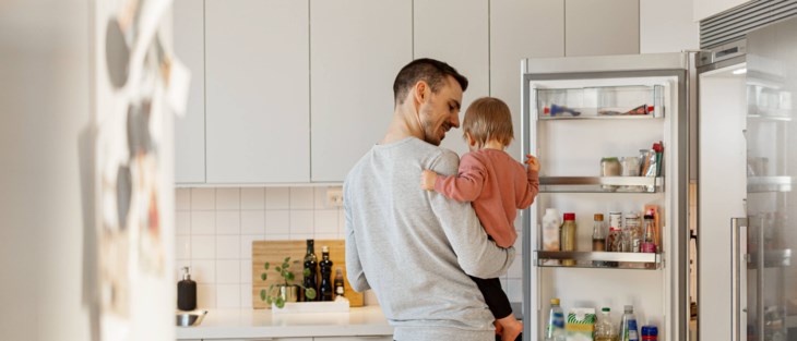 Pappa med barn i famnen letar i kylskåp