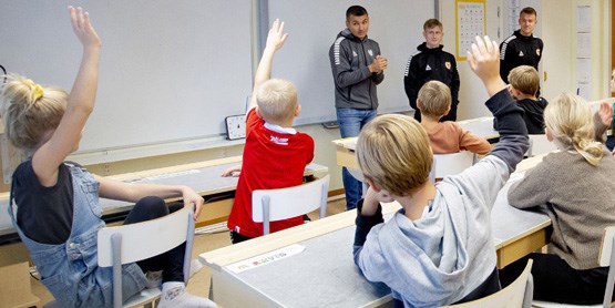 Tre fotbollsspelare framför en skolklass