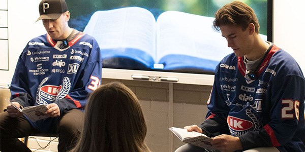 vå hockeyspelare från IK Oskarshamn läser böcker inför en skolklass.