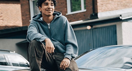 Ung man sitter på en bil och blickar ut