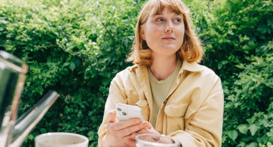 Kvinna sitter i trädgård med sin mobil.