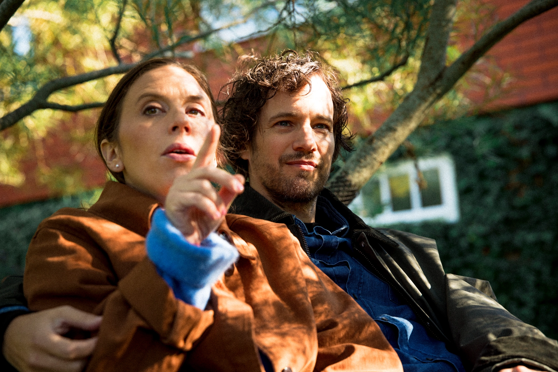 Två personer sitter nära varandra utomhus under trädgrenar.