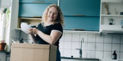 En tjej står i köket och packar upp porslin ur en flyttkartong.