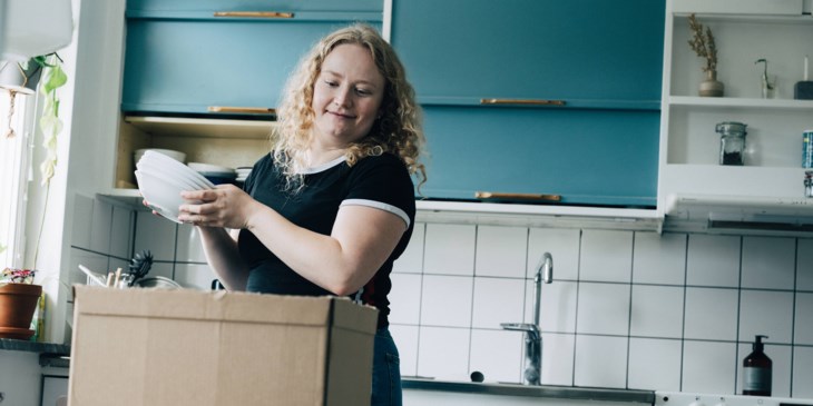 En tjej står i köket och packar upp porslin ur en flyttkartong.