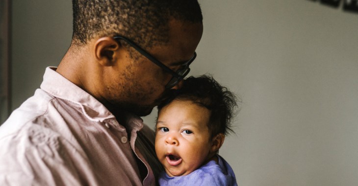 En bebis gäspar stort i förälderns famn.