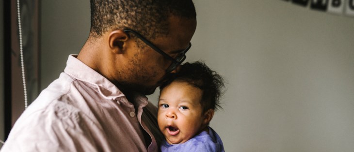 En bebis gäspar stort i sin pappas famn.