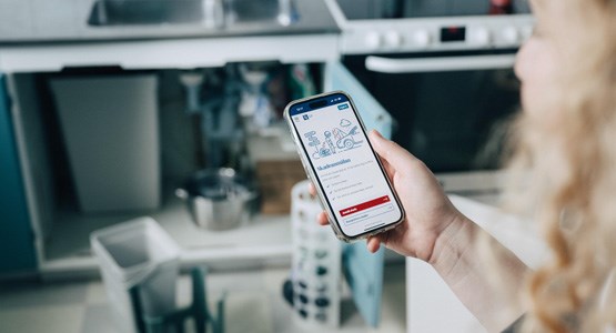 Ung kvinna som kollar i appen i sitt kök.