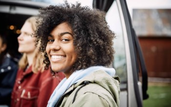 En tjej med krulligt hår står vi en bil och ler mot kameran.