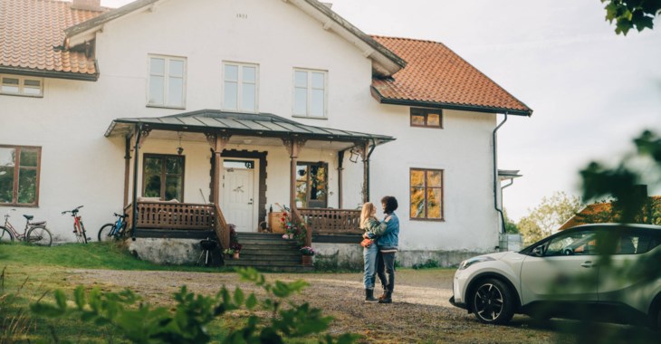 Ett ungt par kramas framför ett stort vitt hus.