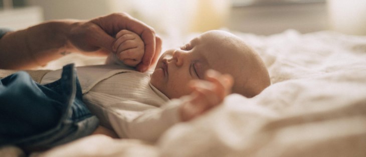 En liten bebis sover gott på mammas och pappas säng.