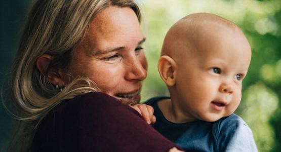 En mamma håller sin lilla bebis, båda ler stort.