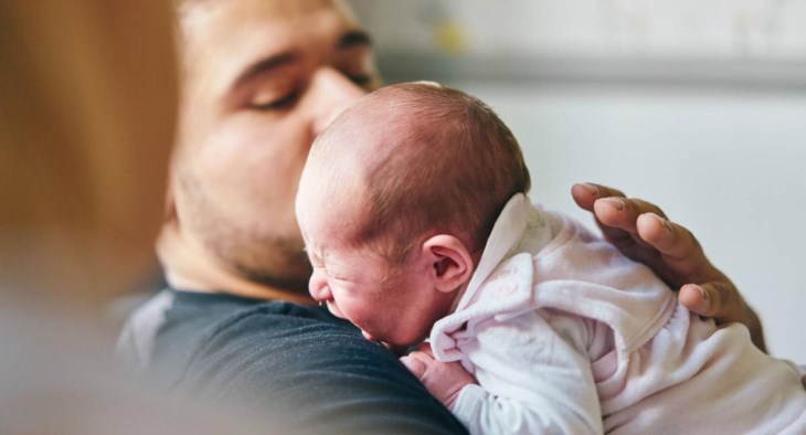 En ledsen bebis gråter vid sin pappas axel.