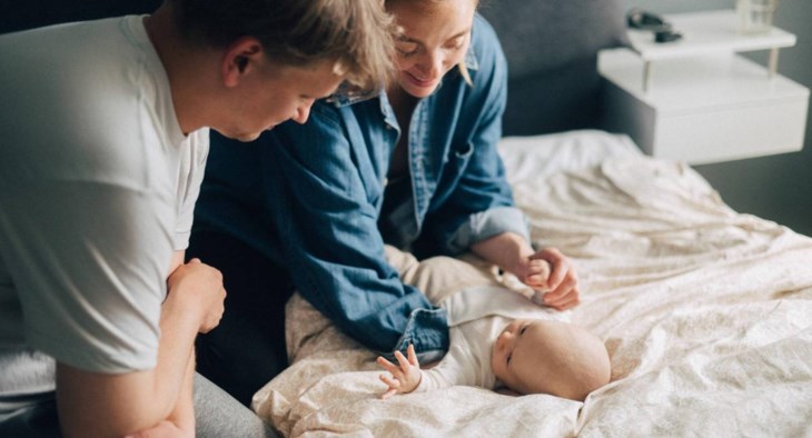 En mamma och pappa myser med sin lilla bebis på sängen.