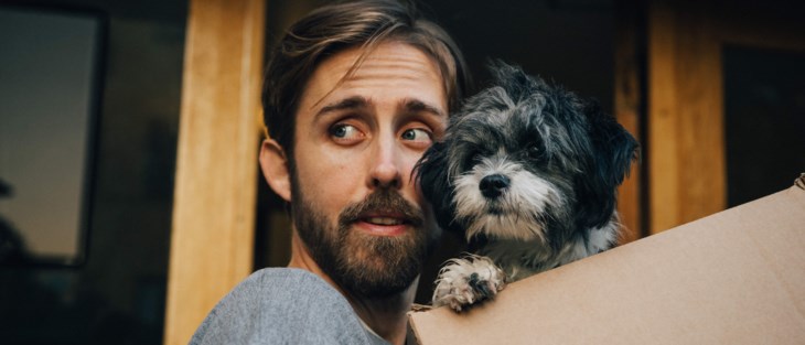 En man bär en flyttkartong och sin lilla vovve.