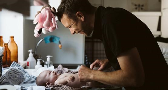 En pappa står vid ett skötbord och byter blöja på sin bebis.