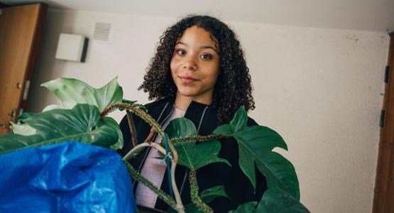 En ung tjej står med en blå kasse och en blomma i famnen, på väg att flytta hemifrån.