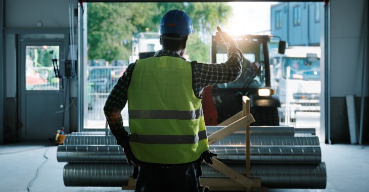 Man i varselkläder och bygghjälm visar en truck in på lager