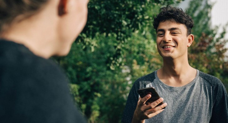 En kille tittar upp från en mobil och ler mot sin kompis.