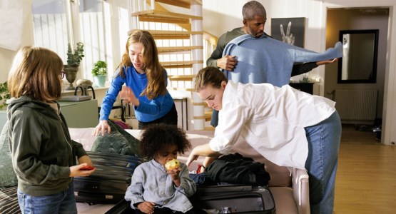 Familj med tre barn packar resväska tillsammans i vardagsrum.