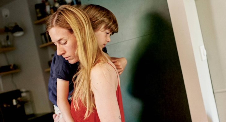 En trött mamma bär sitt barn i famnen.