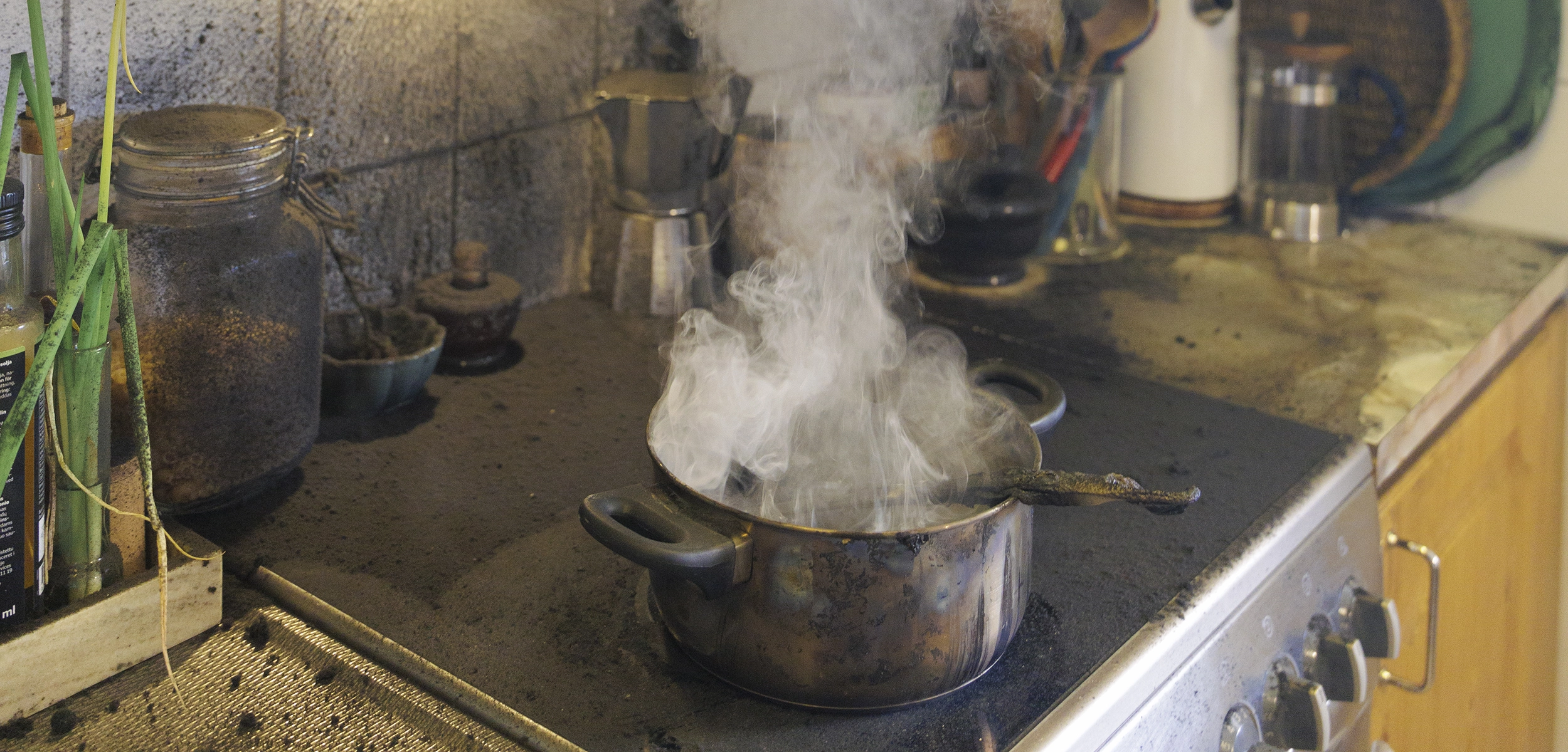 Kastrull som ryker på spis i kök.