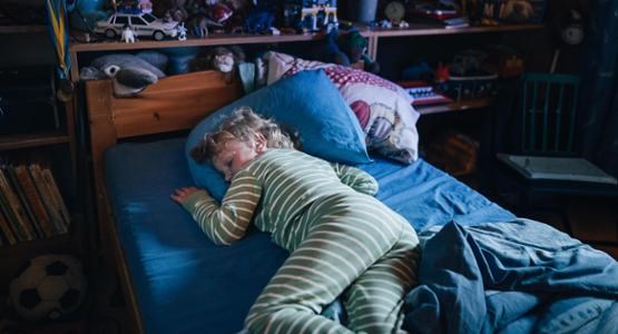 En barn sover själv i sin säng i ett dunkelt sovrum.