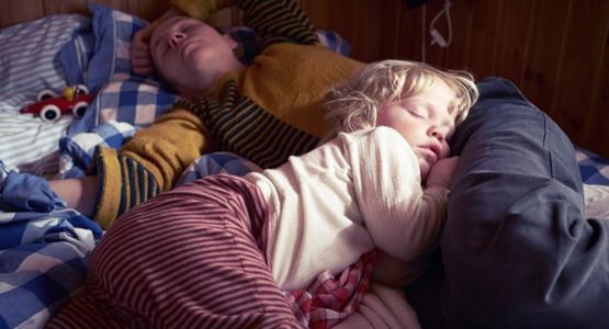 Ett barn sover med huvudet på sin trötta mammas mage.