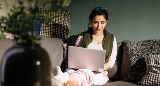 Kvinna sitter i soffa med dator i knät.