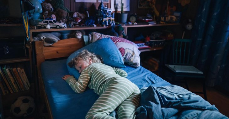 Ett litet barn som sover i sin säng i ett mörkt och nedsläckt rum.